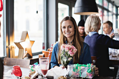 Portrait of smiling woman with gifts at dining table in restaurant