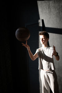 Young man holding ball while standing against wall