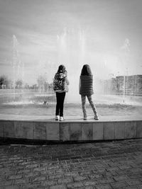 Rear view of sisters standing at fountain