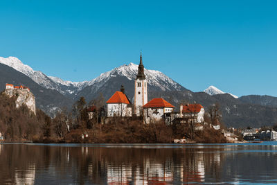 Houses by lake against clear blue sky