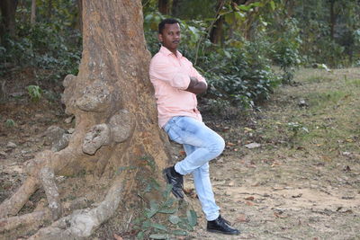 Side view of young man on tree trunk in forest