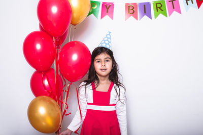 Portrait of a smiling girl with balloons standing against wall
