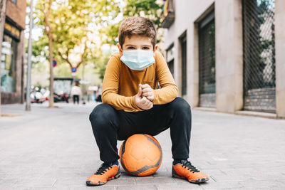 Full length portrait of boy holding ball on street in city