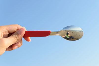 Person holding umbrella against clear blue sky