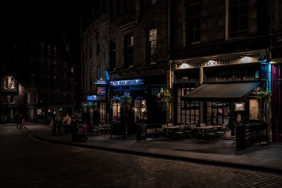 People walking on illuminated street amidst buildings at night