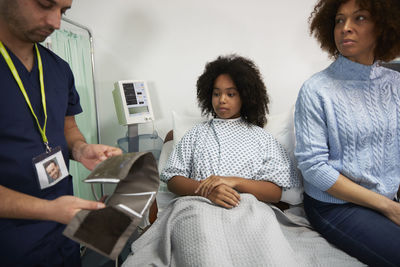 Patient with mother looking at nurse holding blood pressure gauge at hospital