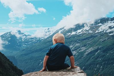 Rear view of man sitting on mountain against sky