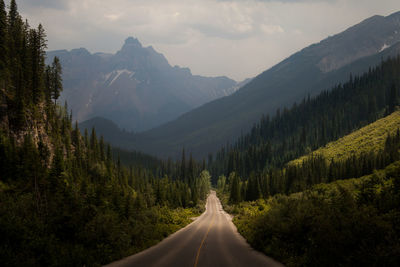 Road amidst trees and mountains against sky