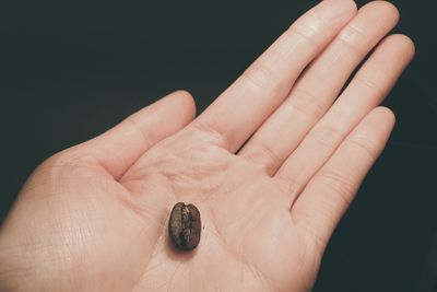 Cropped image of hand holding ring over black background