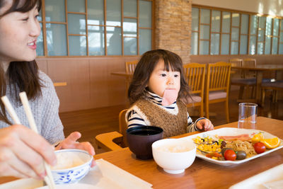 Mother with daughter eating food while sitting in restaurant