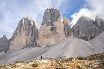 Photographer standing below massive rock towers formation of tre cime, dolomites, italy