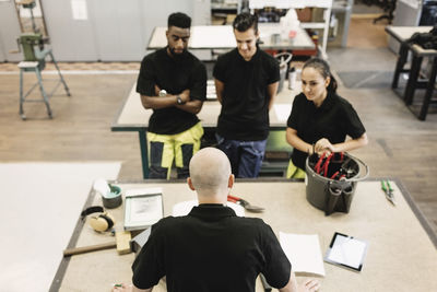 High school teacher teaching students at table in workshop