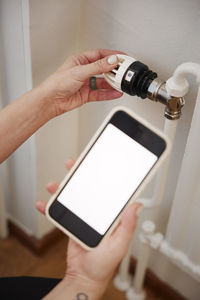 Woman holding phone and using radiator thermostat