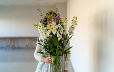 Unrecognizable model hiding her face behind bouquets of white flowers.