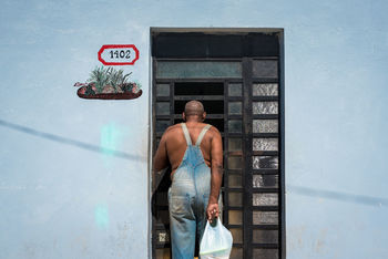 Rear view man with plastic bag standing against closed door of house