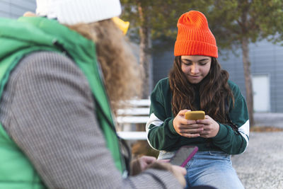 Mother and daughter using mobile phone sitting on bench