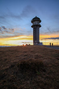 Lighthouse by sea against sky during sunset