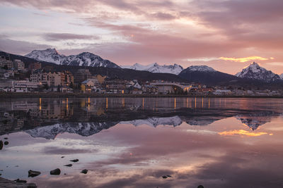 Reflection of buildings and snowcapped mountains in lake during sunset