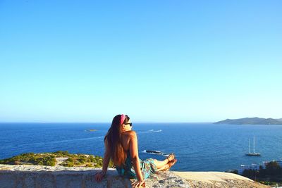 Woman relaxing on retaining wall by sea against sky on sunny day