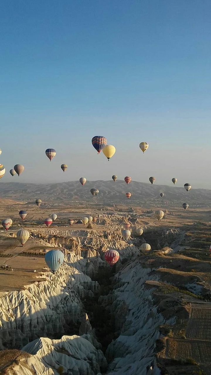 hot air balloon, mid-air, ballooning festival, rock formation, transportation, rock - object, flying, nature, multi colored, outdoors, landscape, scenics, day, adventure, sky, beauty in nature, clear sky, no people, rock hoodoo