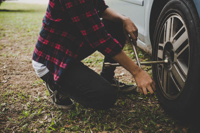 Low section of woman removing tire of car on field