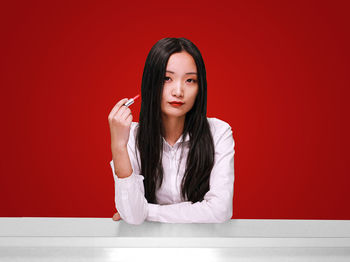 Portrait of young woman with lipstick against red background