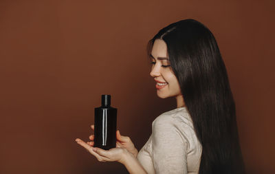 Smiling woman holding shampoo against colored background