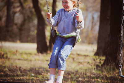 Happy girl swinging against trees