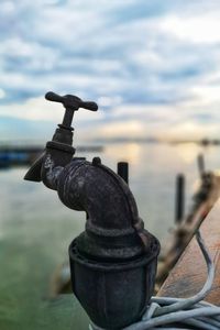 Close-up of old metal railing by sea against sky