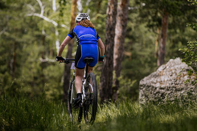 Back woman biking mountain bike on trail forest