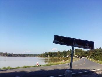 Scenic view of road by lake against clear blue sky