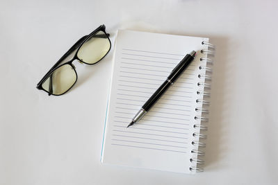 Directly above shot of pen on blank book by eyeglasses at gray background