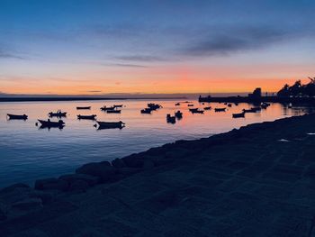 Silhouette boats in sea against sky during sunset