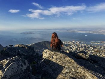 Woman sitting on rock against sky. top of table moutain in cape town, south africa. 