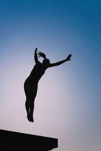 Low angle view of silhouette mid adult woman jumping against clear sky during sunset