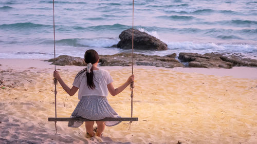 Rear view of woman sitting on swing at beach