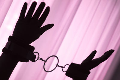Silhouette hands wearing handcuffs against pink curtain