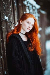 Portrait of young woman standing against tree