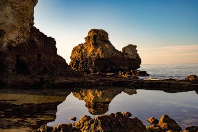 Rock formations by sea against clear sky