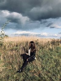 Full length of man sitting on field against sky