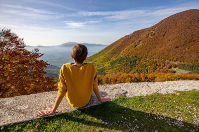 Young woman is sitting and looking at autumn landscape in italy. 