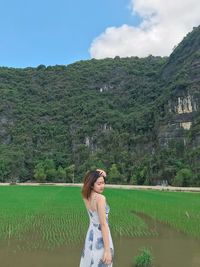 Side view of woman standing at rice paddy against mountains