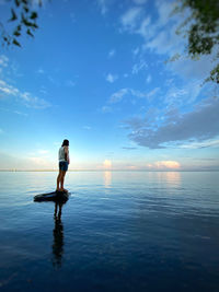 Woman in sea against sky during sunset