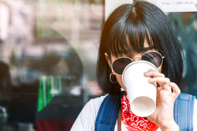Young woman wearing sunglasses drinking coffee in city