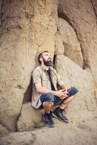 Young man using mobile phone while sitting on rock