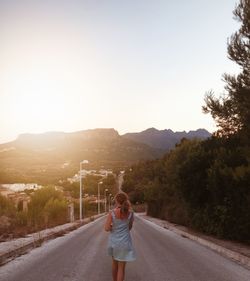 Rear view of man walking on road against clear sky