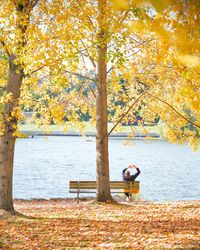 Woman sitting on bench by lake during autumn