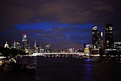 Illuminated buildings by river against sky in city at night