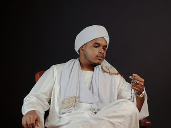 Portrait of young man sitting against black background