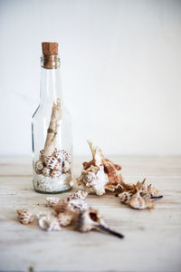 Message in a bottle with seashells on table against wall